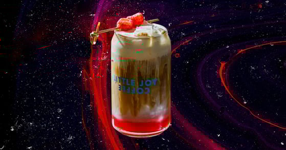 A raspberry danish latte from Little Joy Coffee in a branded glass.