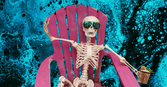 A skeleton wearing sunglasses sits in a pink lawn chair holding a tiki drink against a blue background.