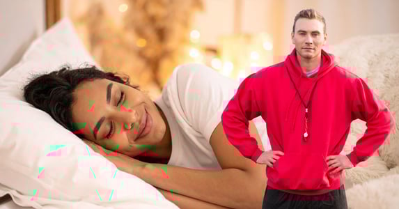 A young woman sleeps peacefully. A male coach in a red hoodie wearing a whistle around his neck stands in the foreground.