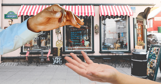 An outstretched hand offers a key to another outstretched hand in front of a cafe. 