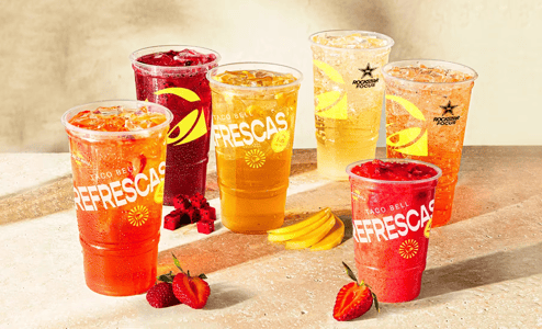 Several plastic cups filled with ice and red, orange, and yellow sodas. The cups read, 'Taco Bell Refrescas.'