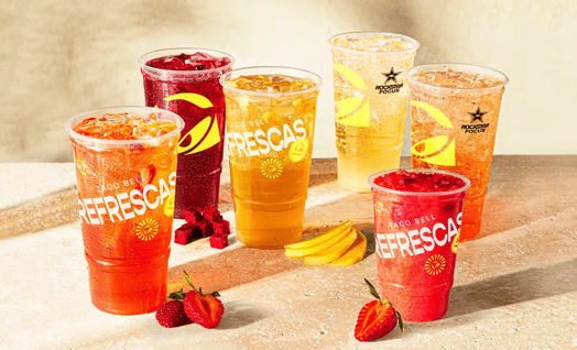 Several plastic cups filled with ice and red, orange, and yellow sodas. The cups read, 'Taco Bell Refrescas.'