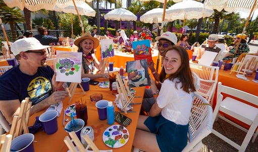 Two men and two women hold up paintings they’ve made of a Taco Bell-inspired tableau.